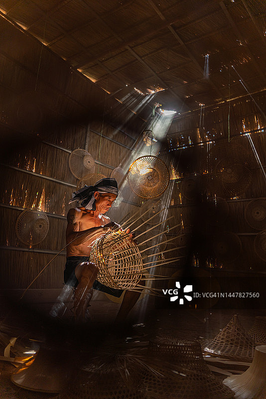 亚洲乡村生活方式：当地成年男性竹编工匠在茅草屋内制作竹篮和帽子图片素材
