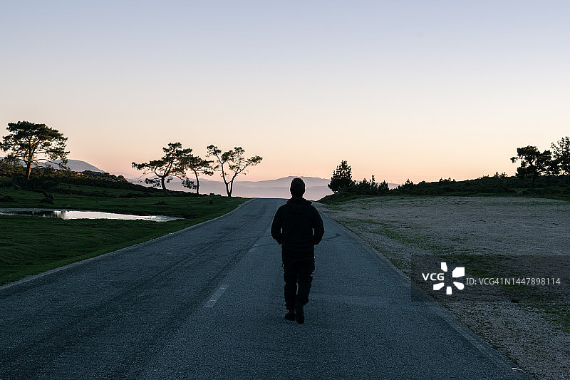 男人在西班牙日落时分沿着空旷的道路走向海岸的背影图片素材