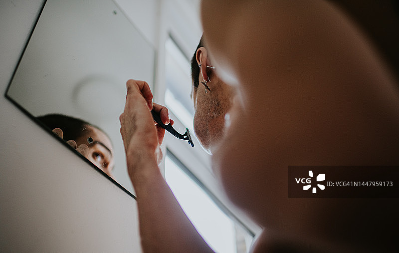 男人在浴室镜子里用手动剃须刀刮胡子图片素材