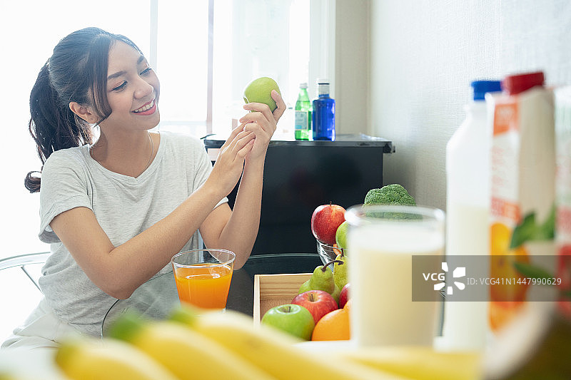 年轻快乐的女人在厨房餐桌旁喝橙汁图片素材