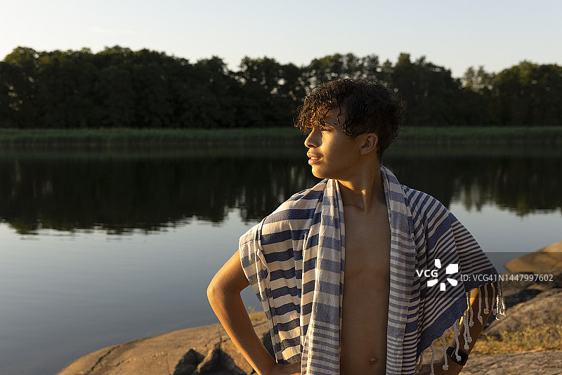 日落时分，裹着毛巾看向湖面的青少年男孩图片素材