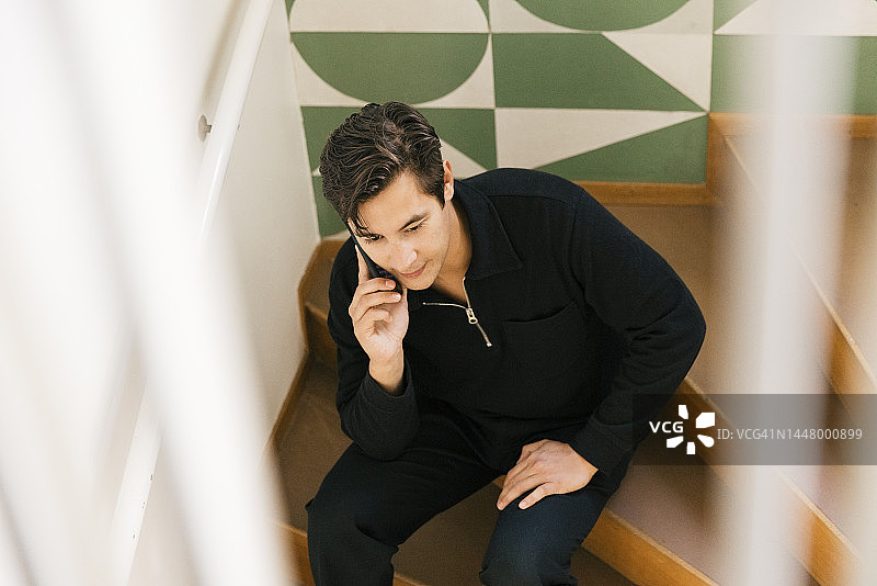 高角度拍摄：男子在家里的台阶上用智能手机图片素材