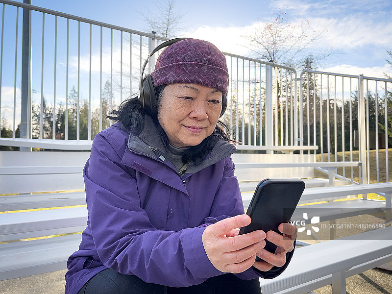 在公园里戴着耳机使用智能手机的60岁以上亚洲女性图片素材