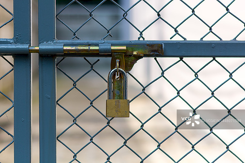 黄铜挂锁锁在铁丝网门上，背景为模糊的电力设备，局部聚焦图片素材