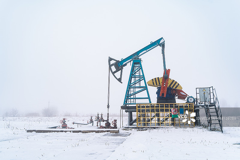 冰雪偏远地区的冰冻钻机，寒冷雾气中农田里工作的积雪抽油机图片素材