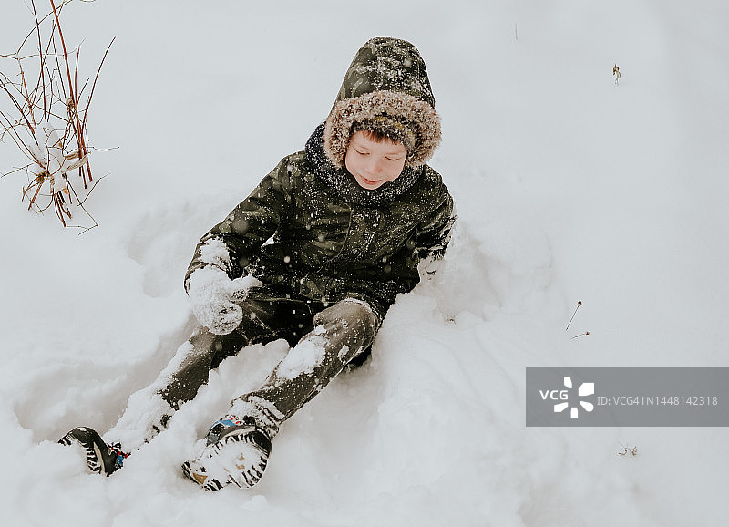 穿着卡其色外套的男孩在雪地里享受冬天图片素材