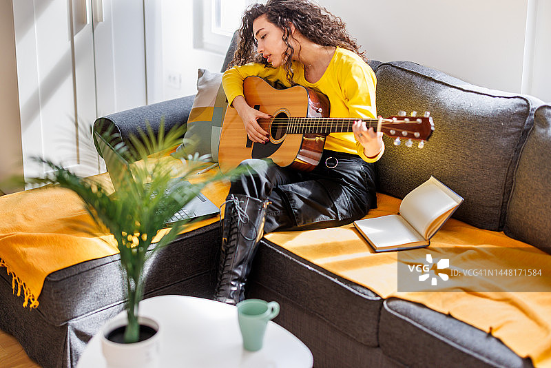 年轻女子在公寓的客厅里上网学习弹吉他图片素材