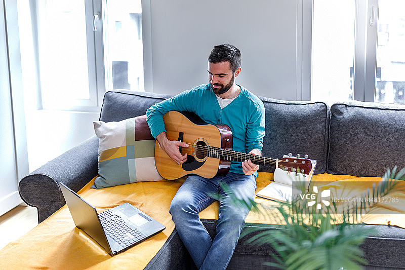 一个年轻男人在家中客厅在网上学习弹吉他图片素材