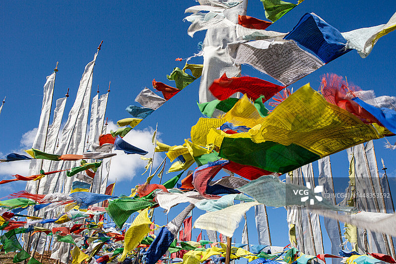 在壮丽的蓝色天空背景下，彩色佛教祈祷旗在风中飘扬的第一视角图片素材