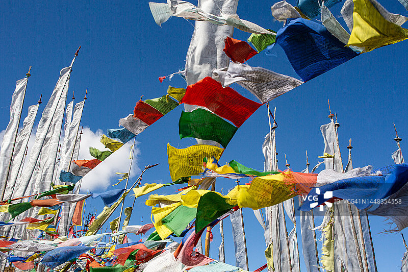 在壮丽的蓝色天空背景下，彩色佛教祈祷旗在风中飘扬的第一视角图片素材