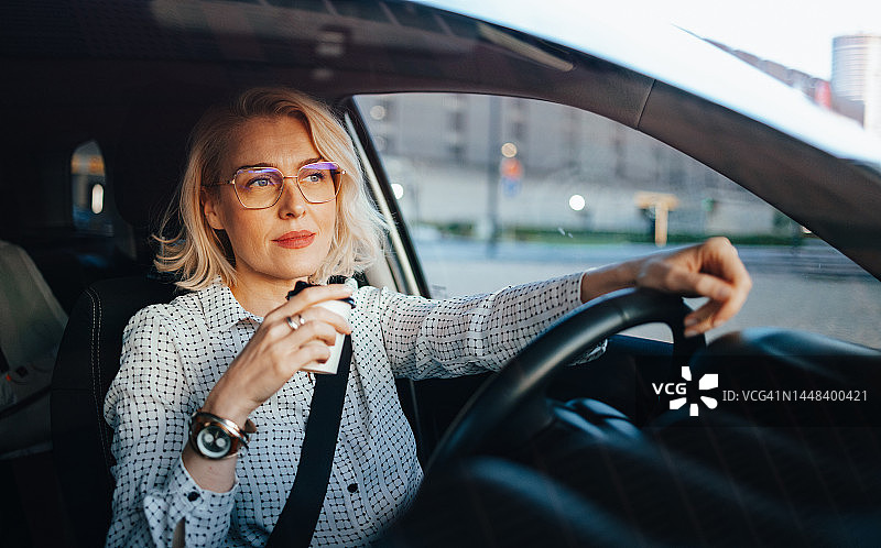 笑容满面的女商人开车时喝咖啡图片素材