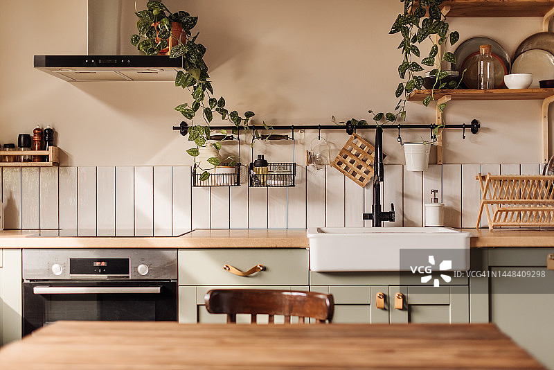 前景是带大理石表面的空厨房岛台，绿色复古台面带抽屉和悬挂的吊灯，罐子里装满了鲜花，背景模糊图片素材