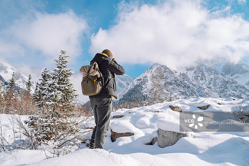 摄影师在雪地里拍摄雪山的照片的背影图片素材