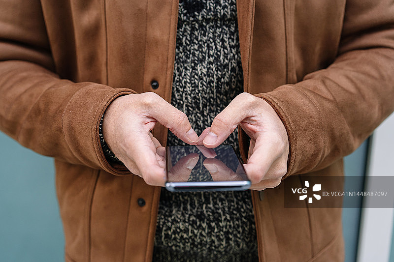 穿着棕色夹克的白人男子在智能手机上打字的特写。图片素材
