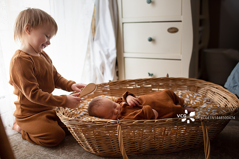 兄妹间的关爱：儿童用木梳为新生婴儿梳头。两个孩子。环保的生活方式和有机的天然产品及婴儿服装。图片素材