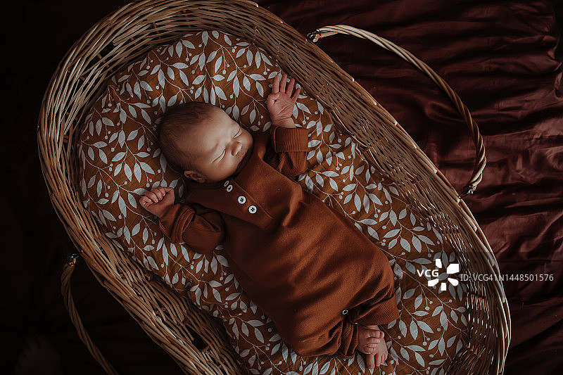 可爱的宝宝躺在复古柳条婴儿床里。环保生活方式图片素材
