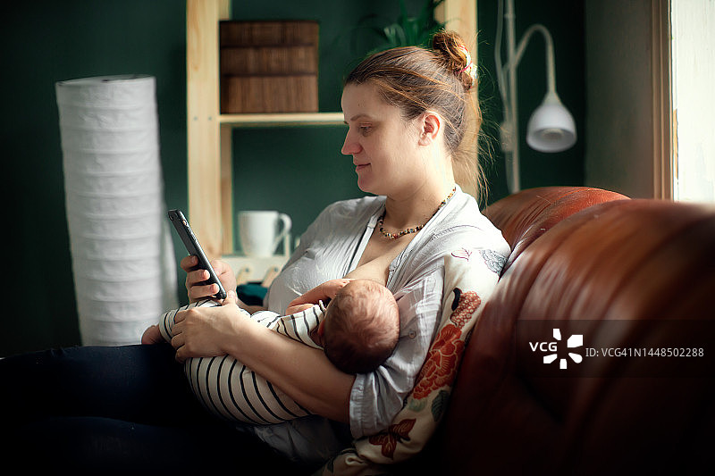 加大码中年母亲给新生儿喂奶，看手机屏幕图片素材