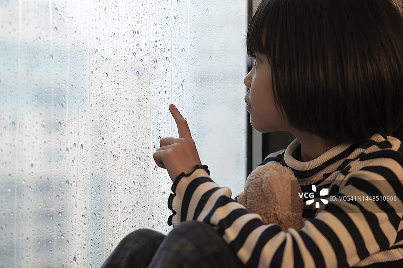 和熊一起隔着窗户看雨的女孩图片素材