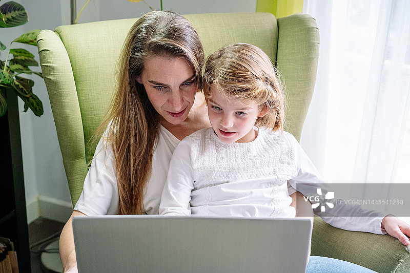 妈妈和女儿在绿色沙发上使用电脑的人像照片图片素材