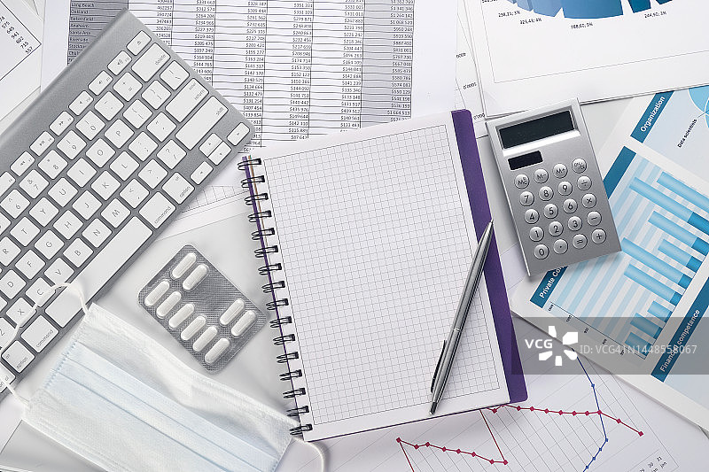 桌面上的图表、柱状图、平板电脑、医用防护口罩和药品，医疗保健行业因价格上涨而造成的损益计算，全球危机概念、医疗行业的经济问题、会计报告图片素材