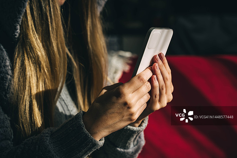 穿着卫衣的女子坐在红色沙发上玩手机图片素材