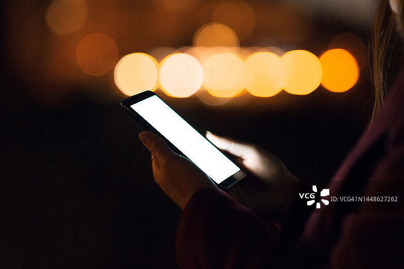 年轻女子在市中心使用智能手机，背景是灯火通明的城市建筑图片素材