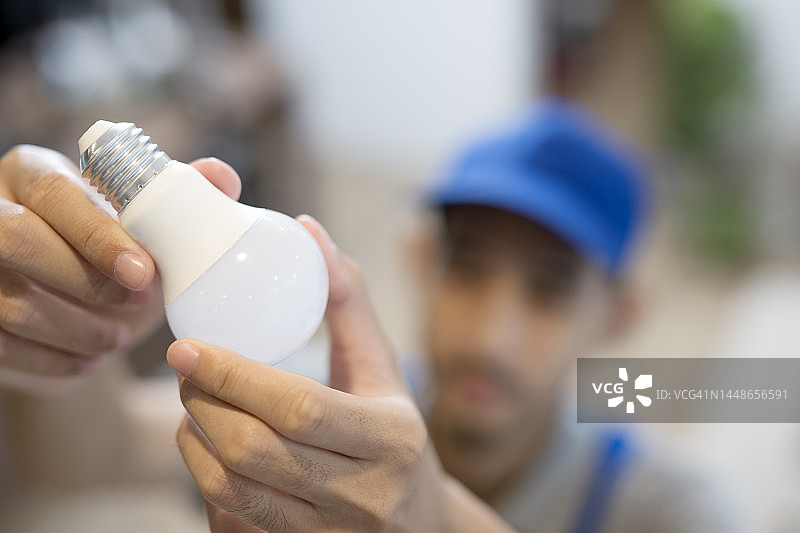 随叫随到的家庭电气维修服务。男性电工在客户家中现场服务时安装或更换天花板灯泡的俯视图图片素材