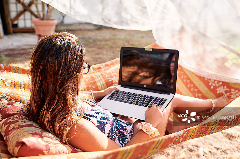 深色头发女孩躺在吊床上使用笔记本电脑图片素材