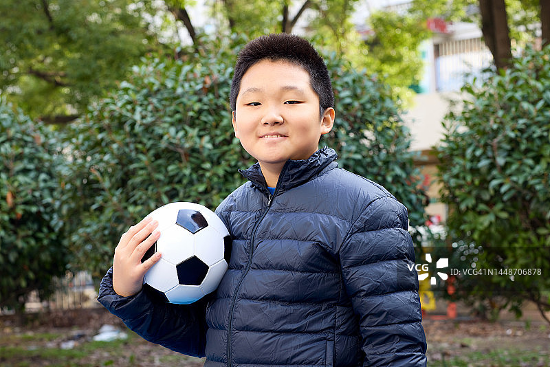 自信地看着镜头抱着足球的快乐男孩图片素材
