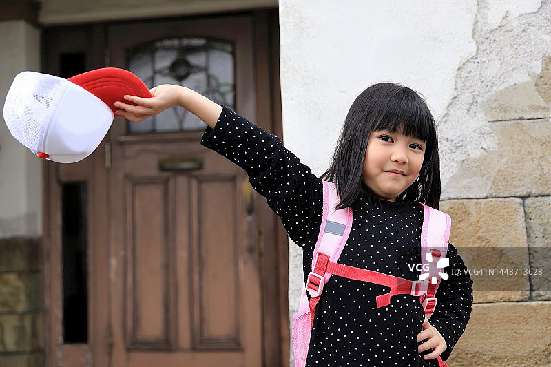 戴着背包和帽子，穿着黑色波点长袖的微笑小女孩肖像图片素材