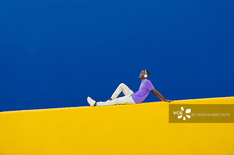 戴着耳机坐在黄色墙壁上的快乐年轻人图片素材