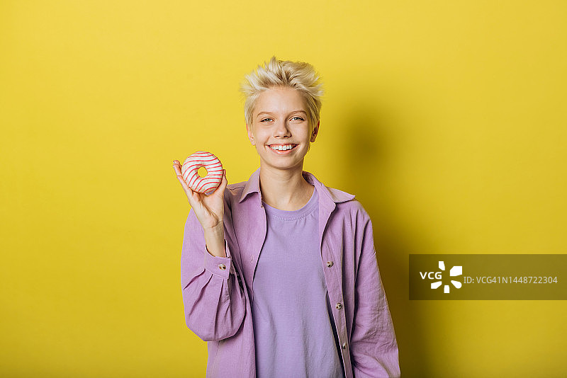 微笑的年轻女人手拿甜甜圈甜点，看向镜头（影棚拍摄）图片素材