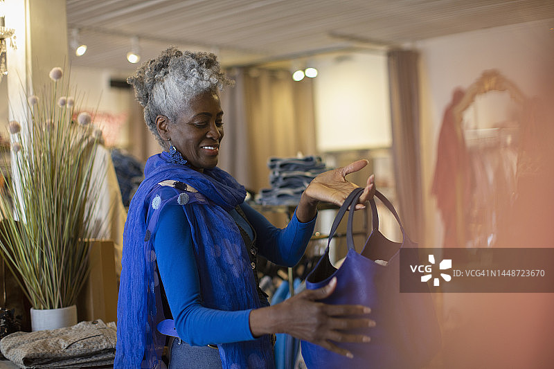 笑容满面的穿着蓝色衣服的老年妇女在商店里看手提包图片素材