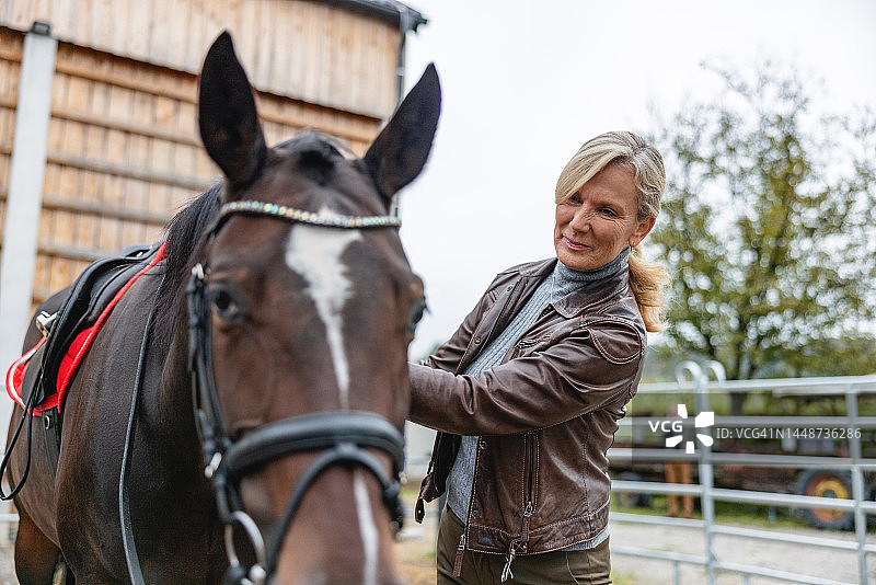 年长的白人妇女看着棕色的马并抚摸它图片素材