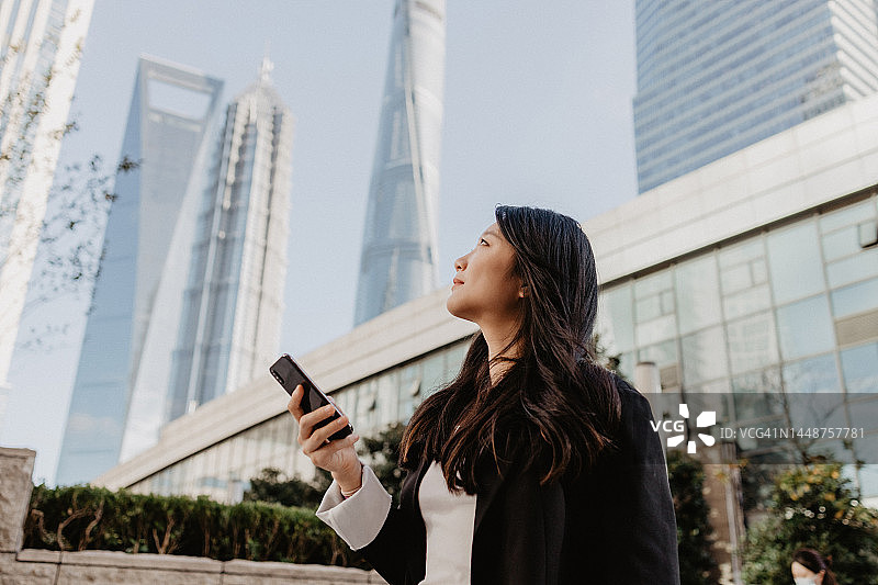 自信的亚洲女商人站在中国上海金融区使用智能手机图片素材