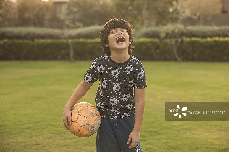 混血（印度-伊朗）8岁男孩玩足球，积极的生活方式。看着镜头微笑图片素材