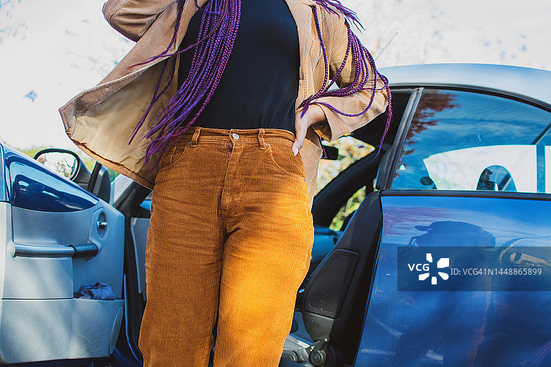 女士走出蓝色汽车，身穿棕色灯芯绒裤子图片素材