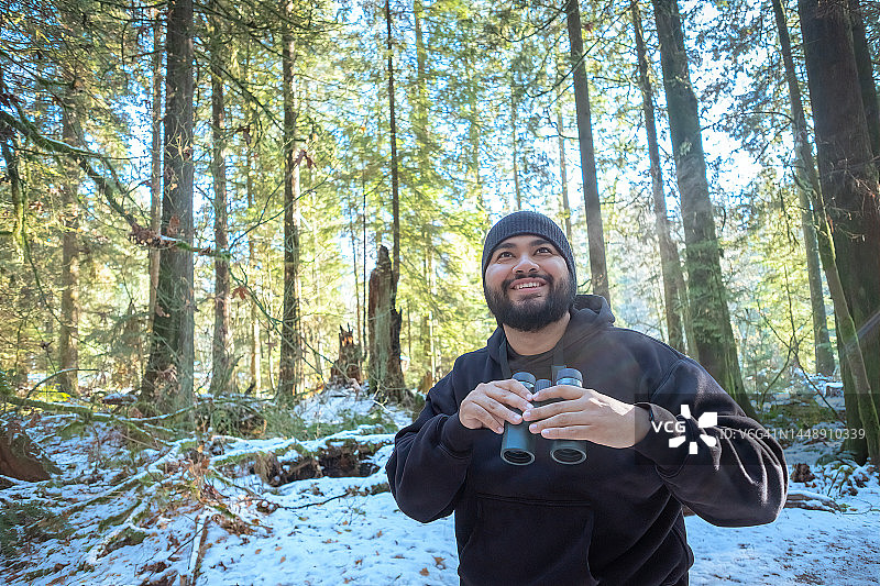 在雪后的冬季森林里用双筒望远镜微笑观鸟的拉丁裔男人图片素材