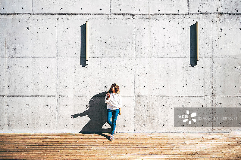 在阳光明媚的日子里，靠在灰色水泥墙上使用手机的现代女性图片素材