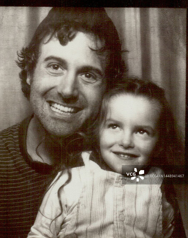 年轻的父亲和三岁女儿在照相亭里微笑的肖像图片素材