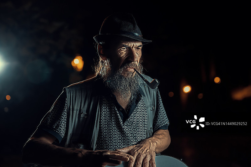 戴帽子的愤怒的鼓手在晚上抽烟斗图片素材