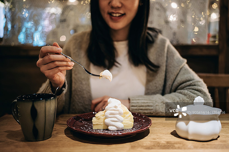 年轻的亚洲女性在咖啡馆享用美味奶油蛋糕的局部照片。用一块蛋糕和咖啡满足她的甜食爱好。拥有轻松和无忧无虑的时刻。人，食物和生活方式概念图片素材