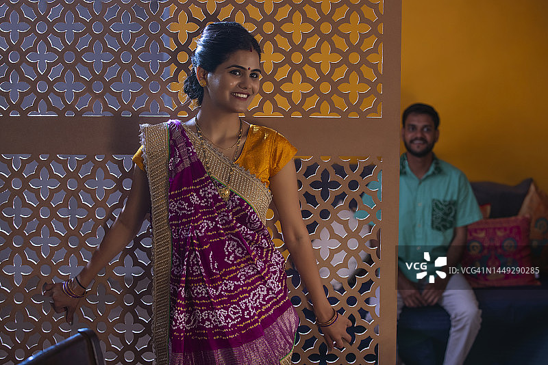 站立的古吉拉特邦微笑女性及其丈夫坐在身后的肖像图片素材