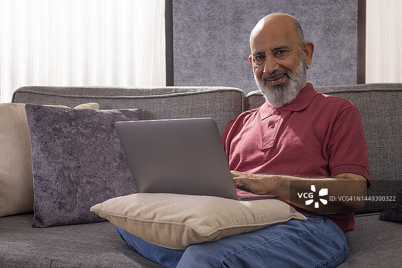 在家坐在沙发上使用笔记本电脑的老年男人画像图片素材