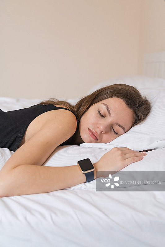 年轻女子戴着智能手表在床上睡觉，跟踪睡眠图片素材