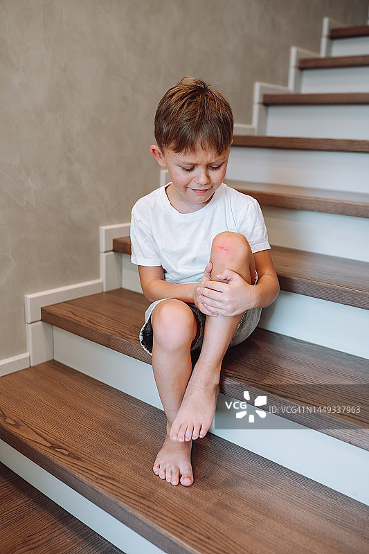 膝盖受伤。悲伤的男孩在楼梯上受伤后抱着他的腿图片素材