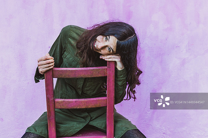 微笑的女人坐在椅子上，淡紫色背景图片素材