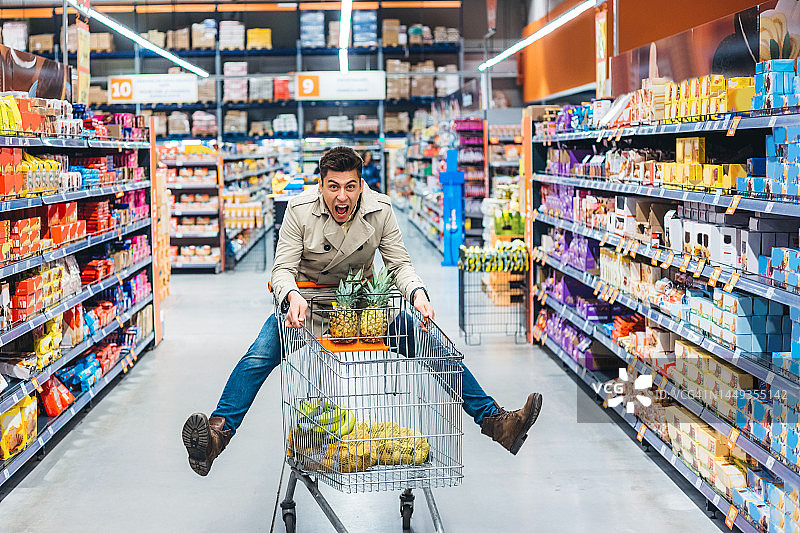 年轻男人在杂货店里乘坐购物车图片素材