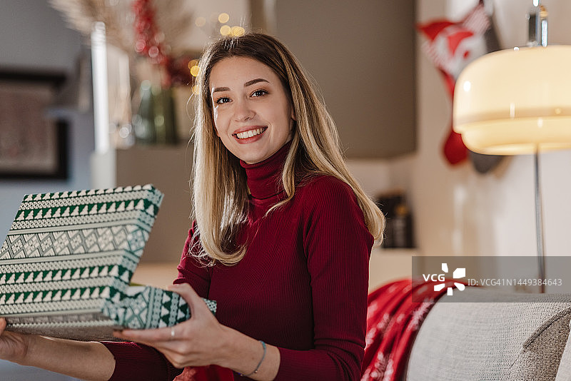 在客厅打开圣诞礼物的年轻金发女子图片素材