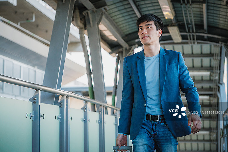 身穿西装、携带行李，在BTS轻轨铁路站台上行走去上班的亚洲商人图片素材